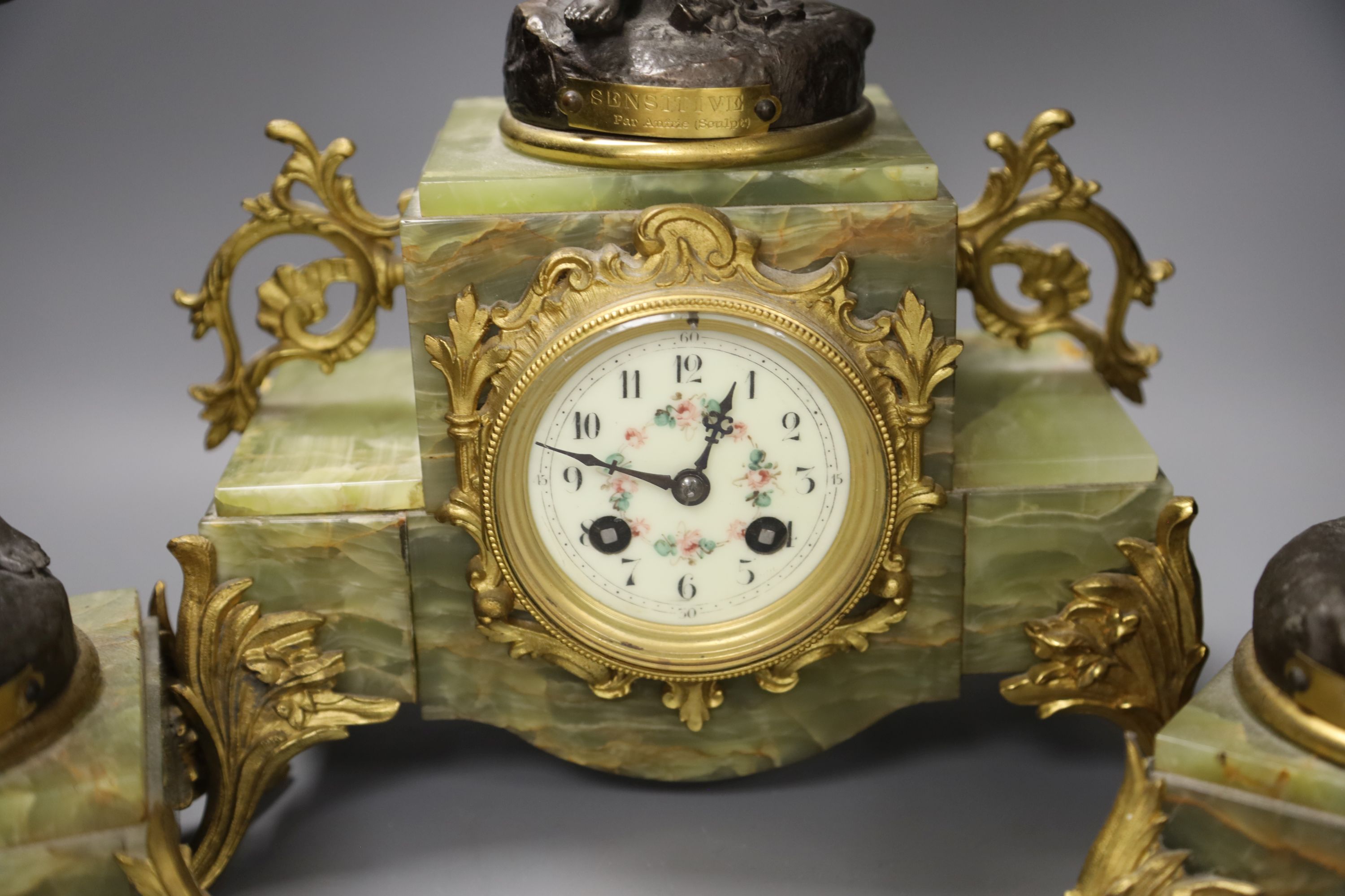 A French onyx and spelter figural clock garniture after Ferrand, plaques read Improvisateur Prisonniere and Sensitive, height 50cm